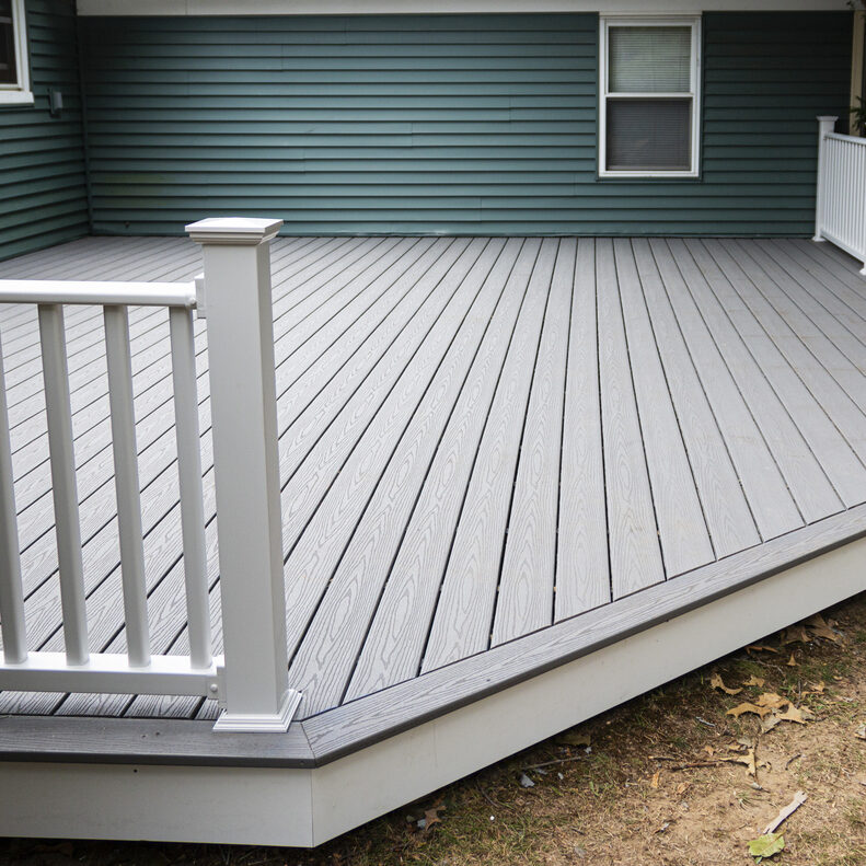 New composite deck on the back of a house with green vinyl siding.with whie railings.