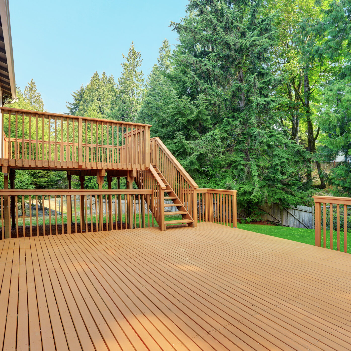 Backyard view of grey rambler house with upper and lower decks and green lawn. Kirkland, WA, USA.